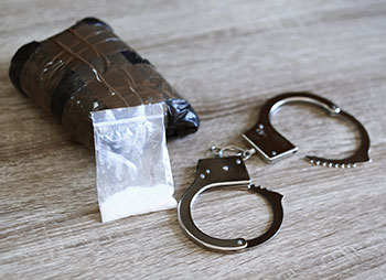 Drugs and handcuffs on table, symbolizing drug charges and criminal consequences - Law Office Of Greg Webb